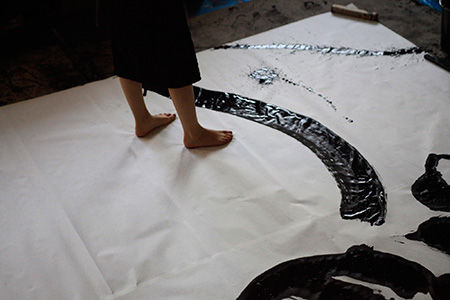 Japanese calligraphy shodo artist, barefoot on a large canvas splashing black inc